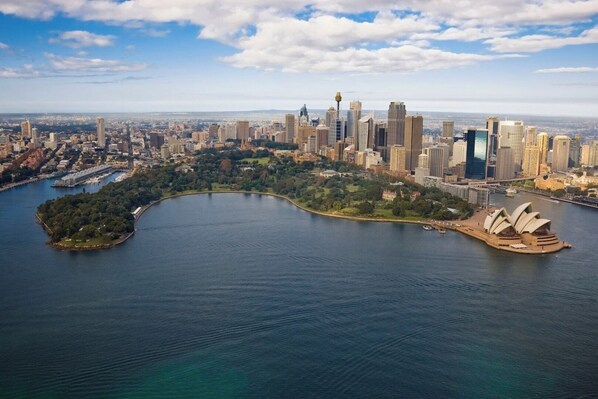 An aerial view of a city with a prominent waterfront, including a large body of water and a distinctive opera house.