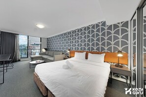 A hotel room with a large bed, a sofa, a desk, and a view of the city.