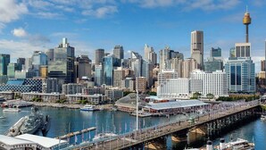 A city skyline with modern skyscrapers, a prominent tower, and a waterfront area with boats and a bridge.