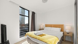A hotel room with a large window, a bed with a headboard, two bedside tables with lamps, and a flat-screen TV.