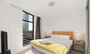 A hotel room with a large window, a bed with a headboard, two bedside tables with lamps, and a flat-screen TV.