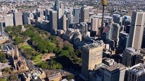 A cityscape with modern high-rise buildings, a prominent tower, and a park area with trees. - KozyGuru |  Rozelle | Bridge View with Carpark (Rozelle)