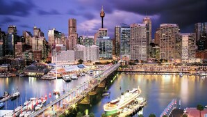 A city skyline with a prominent tower and a waterfront promenade with boats.