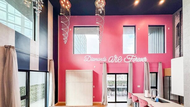 Un intérieur moderne avec un mur rose, un canapé agrémenté de coussins décoratifs, un coin bar avec des tabourets et une grande fenêtre.
