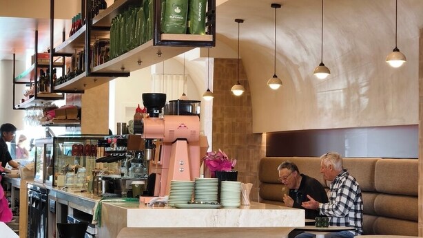 Interior de café moderno com balcão central, área de estar e luminárias pendentes.