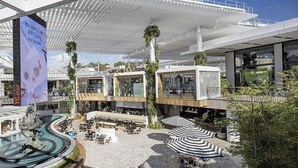 Um átrio moderno de hotel com um elemento central de água, áreas de estar ao ar livre e um shopping Westfield.