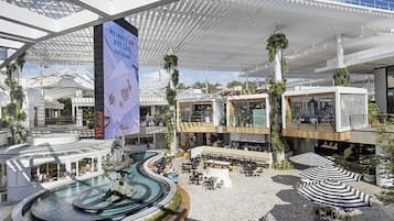 A modern hotel atrium with a central water feature, outdoor seating areas, and a Westfield shopping mall.