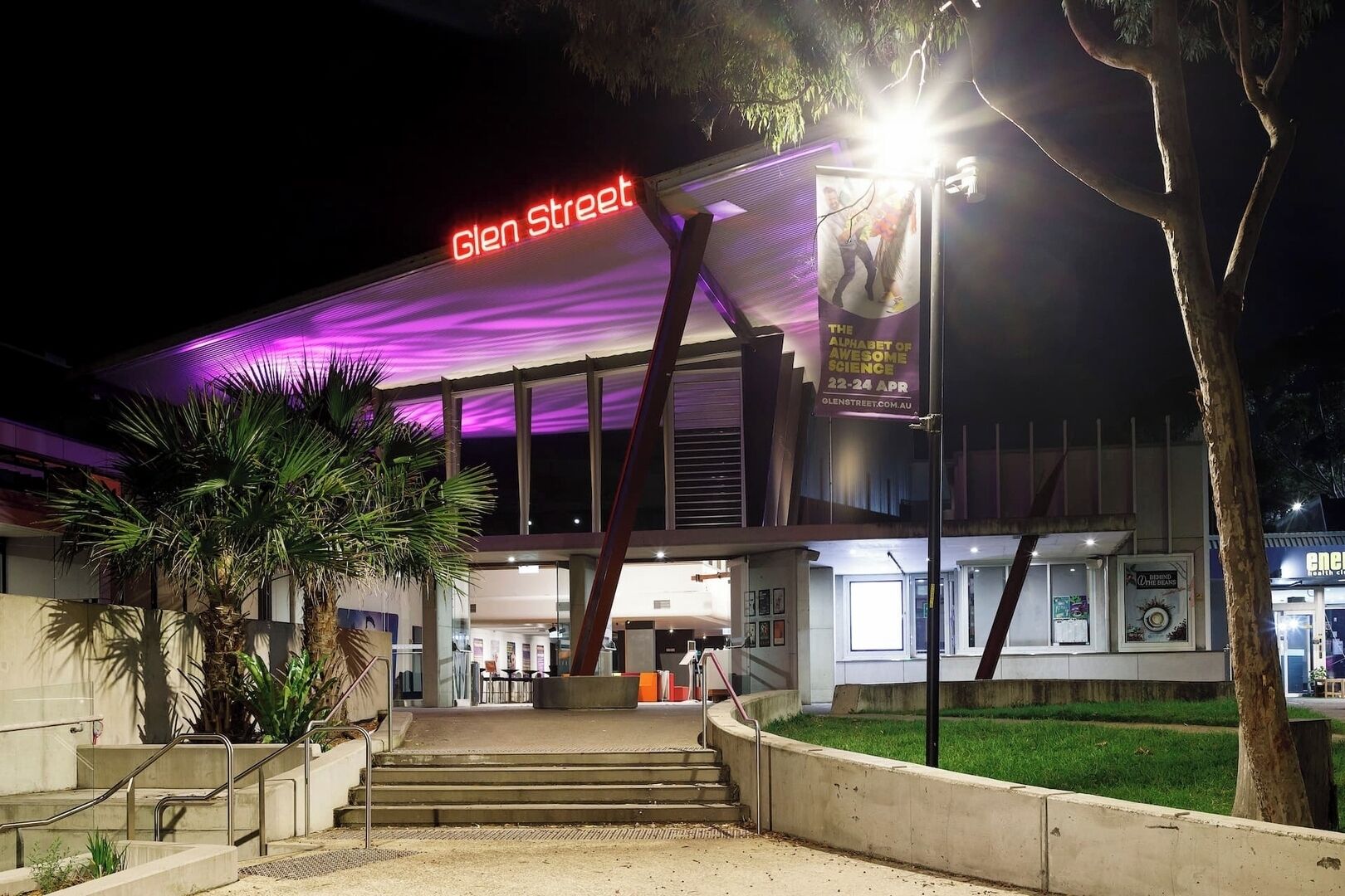 A modern building with a prominent 'Glen Street' sign, featuring a digital display and a large poster advertising 'The Alphabet of Awesome Science' event.