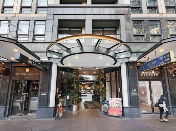 Entrada de hotel moderna con un toldo de vidrio curvo, un atrio central y varias tiendas, incluyendo una tienda de artículos de cuero.