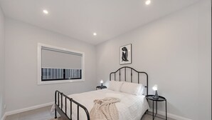 A bedroom with a bed, bedside tables, a window, and a wall-mounted picture.