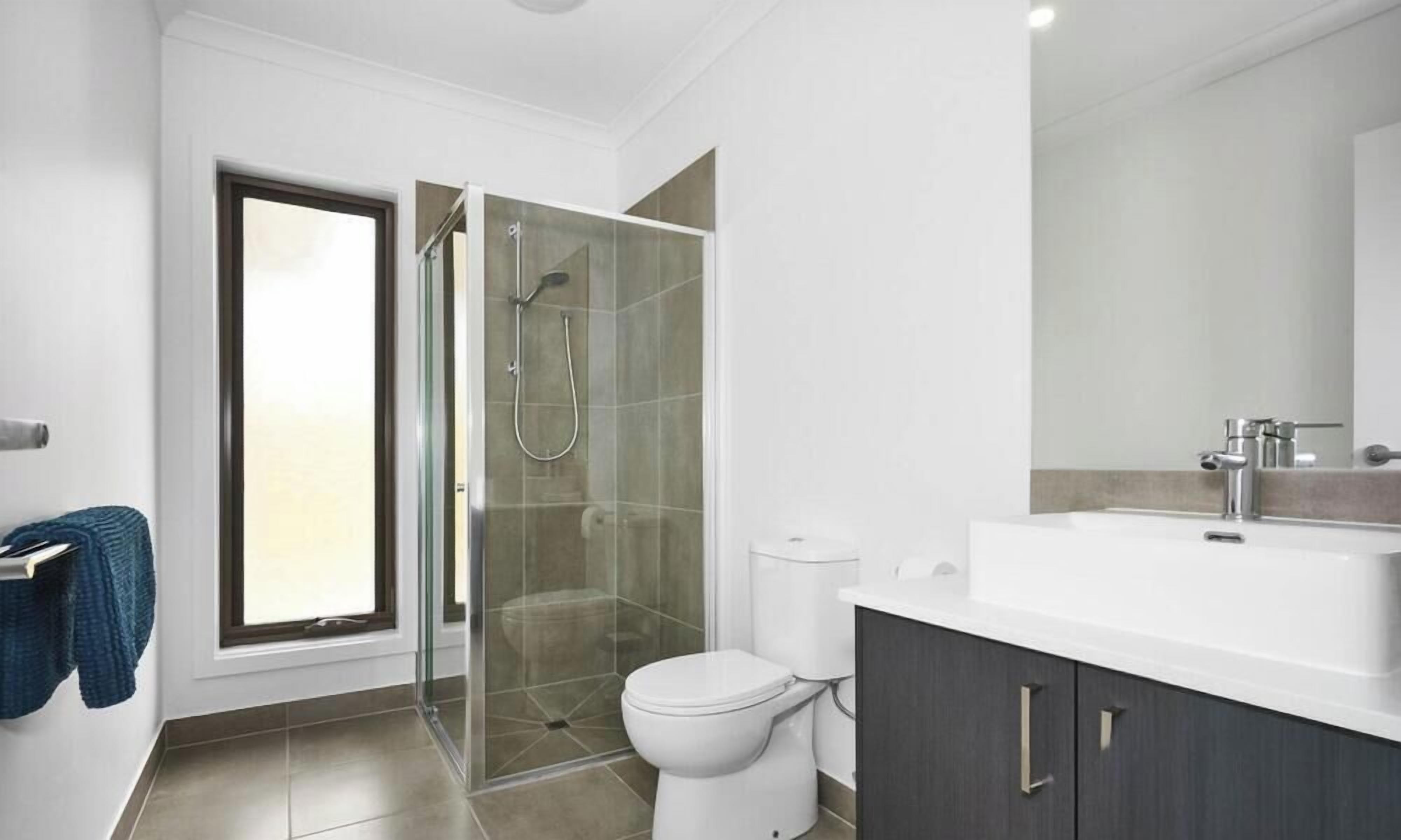 A modern bathroom with a glass-enclosed shower, a white toilet, and a large mirror above a white sink.