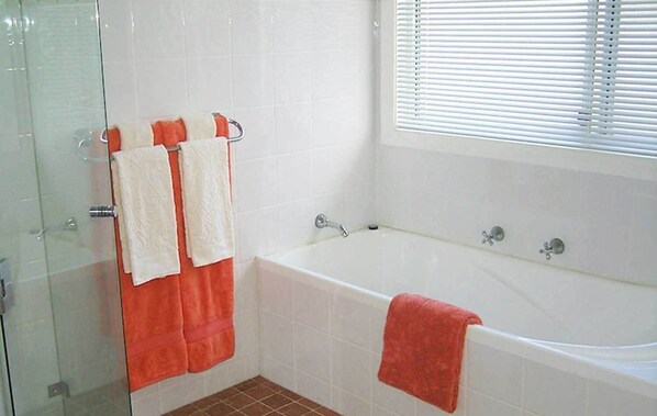 A bathroom with a bathtub, a glass shower enclosure, and a window with blinds.