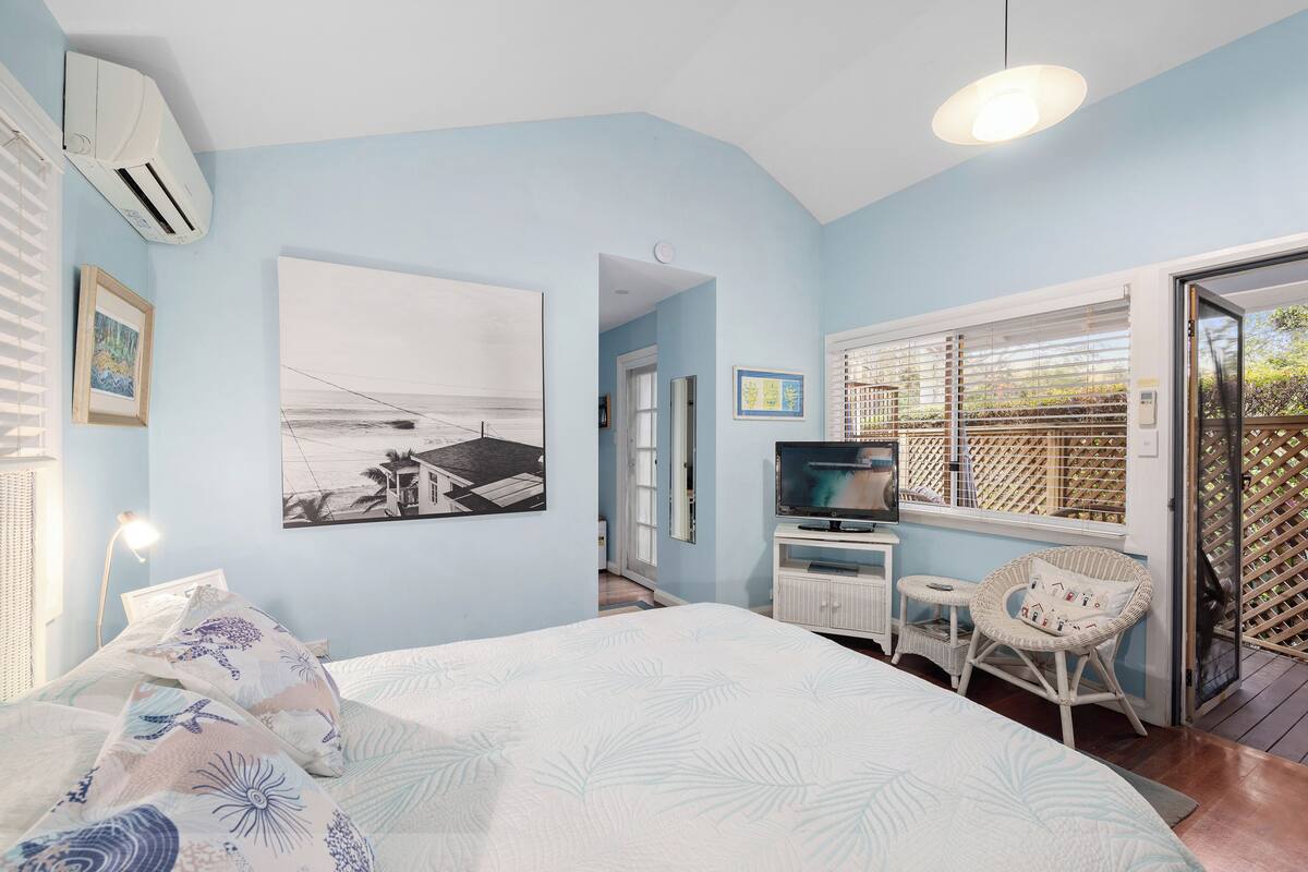A bedroom with a bed, a television, a window with blinds, and a door leading to a balcony.