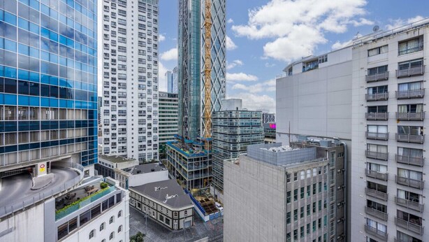 A modern urban skyline with high-rise buildings, including a distinctive glass skyscraper and a construction site with a crane. - 3 Double 1 Single 2 Sofa Beds apartment (Auckland)