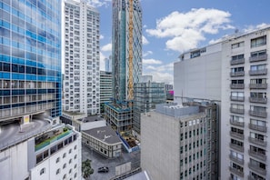 A modern urban skyline with high-rise buildings, including a distinctive glass skyscraper and a construction site with a crane. - 3 Double 1 Single 2 Sofa Beds apartment (Auckland)
