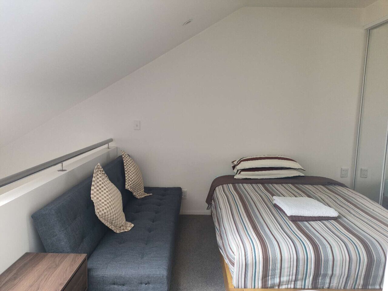 A small, modern bedroom with a sofa bed and a single bed, both with striped bedding.