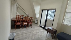 A high-ceilinged room with a dining area featuring a wooden table and chairs, a small bench, and a sliding glass door leading to a balcony. - 3 Double 1 Single 2 Sofa Beds apartment (Auckland)