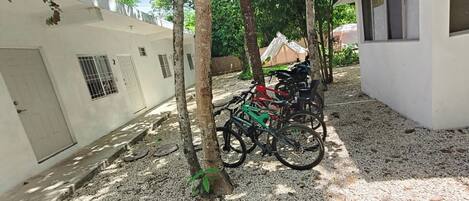 A courtyard with bicycles parked near trees, a white building with barred windows, and a tent in the background.