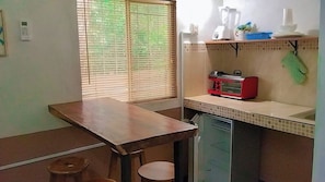Uma cozinha compacta com uma mesa de madeira, uma torradeira vermelha e um liquidificador sobre o balcão.