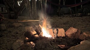 A campfire with rocks and logs, surrounded by trees and string lights. - Bacalar inn (Bacalar)