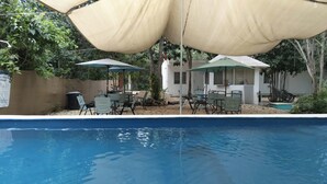A swimming pool with lounge chairs and umbrellas, surrounded by a sandy area and greenery. - Bacalar inn (Bacalar)