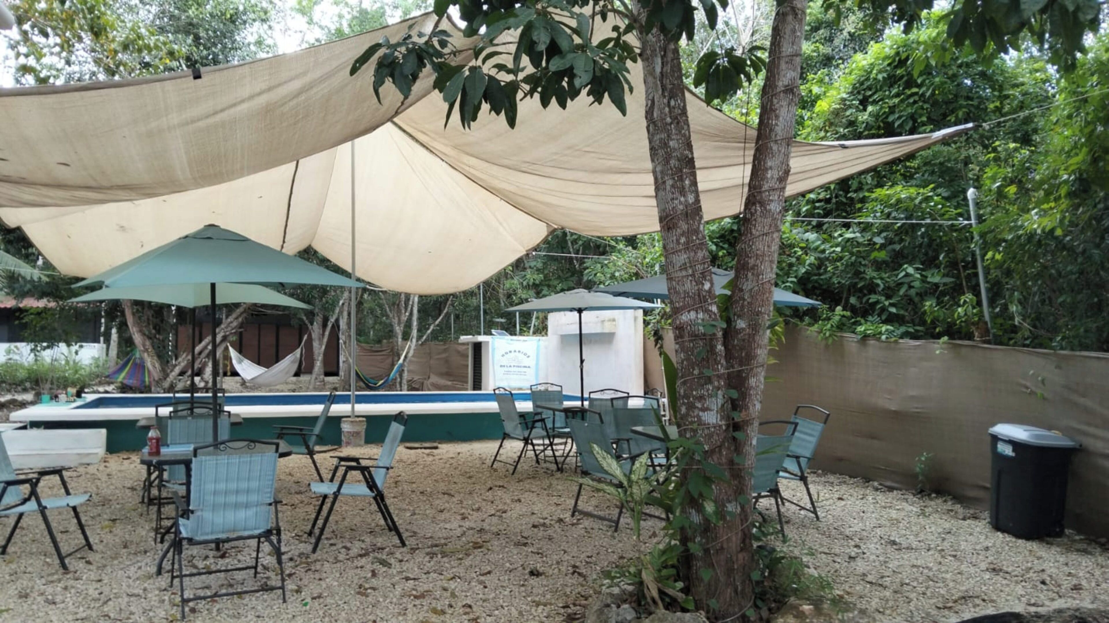 An outdoor seating area with tables and chairs, a pool, and a shaded canopy.