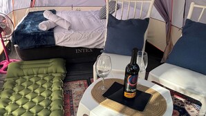 A cozy tented room with a bed, green cushioned seating, a small table with a bottle and glasses, and a patterned rug. - Bacalar inn (Bacalar)