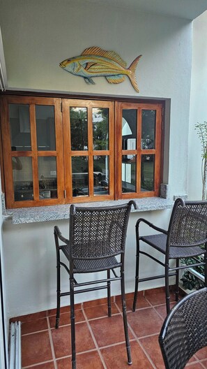 Ein Zimmer mit Fensterblick auf einen Garten, zwei Korbstühle und einem Wandbild mit Fischmotiven.