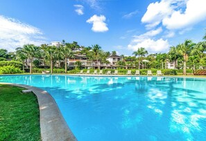 Ein Swimmingpool mit Liegestühlen, umgeben von Grünflächen und Gebäuden.