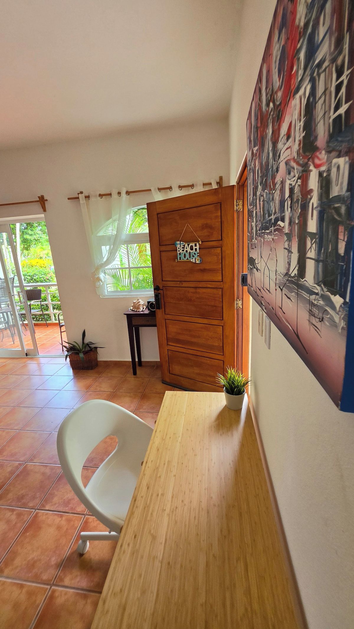 Une pièce avec une porte en bois portant l’inscription « MAISON DE PLAGE », une chaise blanche, une petite table et une plante en pot.