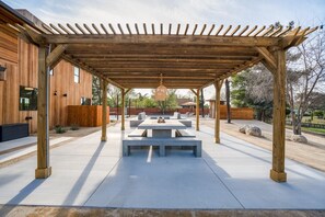 Une terrasse extérieure dotée d’une pergola en bois, de tables en béton et de bancs.