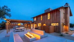 A modern wooden house with a patio area featuring a fire pit, outdoor seating, and a pergola. - Cedar House | Pickleball, Saltwater Pool, Sauna (Paso Robles)