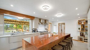 A modern kitchen with a large island, bar stools, a coffee machine, and a view of the outdoors. - Cedar House | Pickleball, Saltwater Pool, Sauna (Paso Robles)