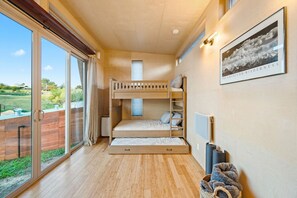 Une chambre avec un lit superposé, une grande fenêtre, un tableau encadré au mur et un petit tapis.