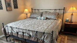 A bed with a metal frame and patterned bedding, two bedside tables with lamps, and a patterned rug on a wooden floor. - Aimee's Retreat on Robinson! Convenient to University of OK in Norman! (Moore)