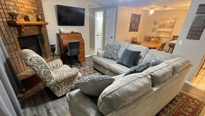A living room with a fireplace, a sofa set, a patterned armchair, a television, and a dining area in the background. - Aimee's Retreat on Robinson! Convenient to University of OK in Norman! (Moore)