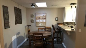 A dining area with a round table and chairs, a painting on the wall, and a kitchen area with a countertop and cabinets. - Aimee's Retreat on Robinson! Convenient to University of OK in Norman! (Moore)