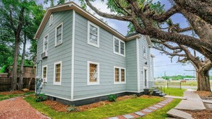 Une maison à deux étages avec un porche à l’avant, un grand arbre et une pelouse bien entretenue.