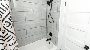 Une salle de bain avec une baignoire blanche, une pomme de douche et une étagère en verre.