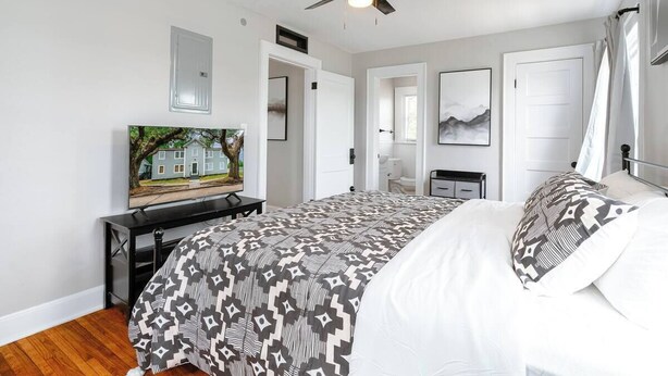 Une chambre avec un lit, un ventilateur de plafond, un bureau avec un ordinateur et un téléviseur.