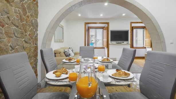 Une table de petit-déjeuner installée devant un mur en pierre, avec des chaises, et une télévision en arrière-plan.