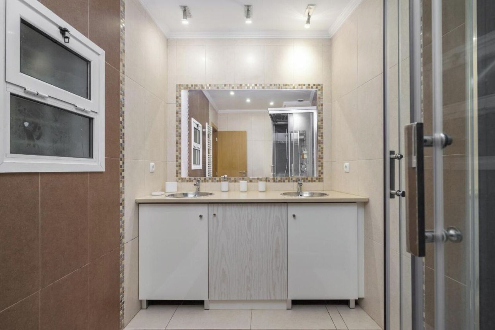 Une salle de bain moderne avec un meuble-lavabo à deux vasques, un grand miroir et un espace douche.