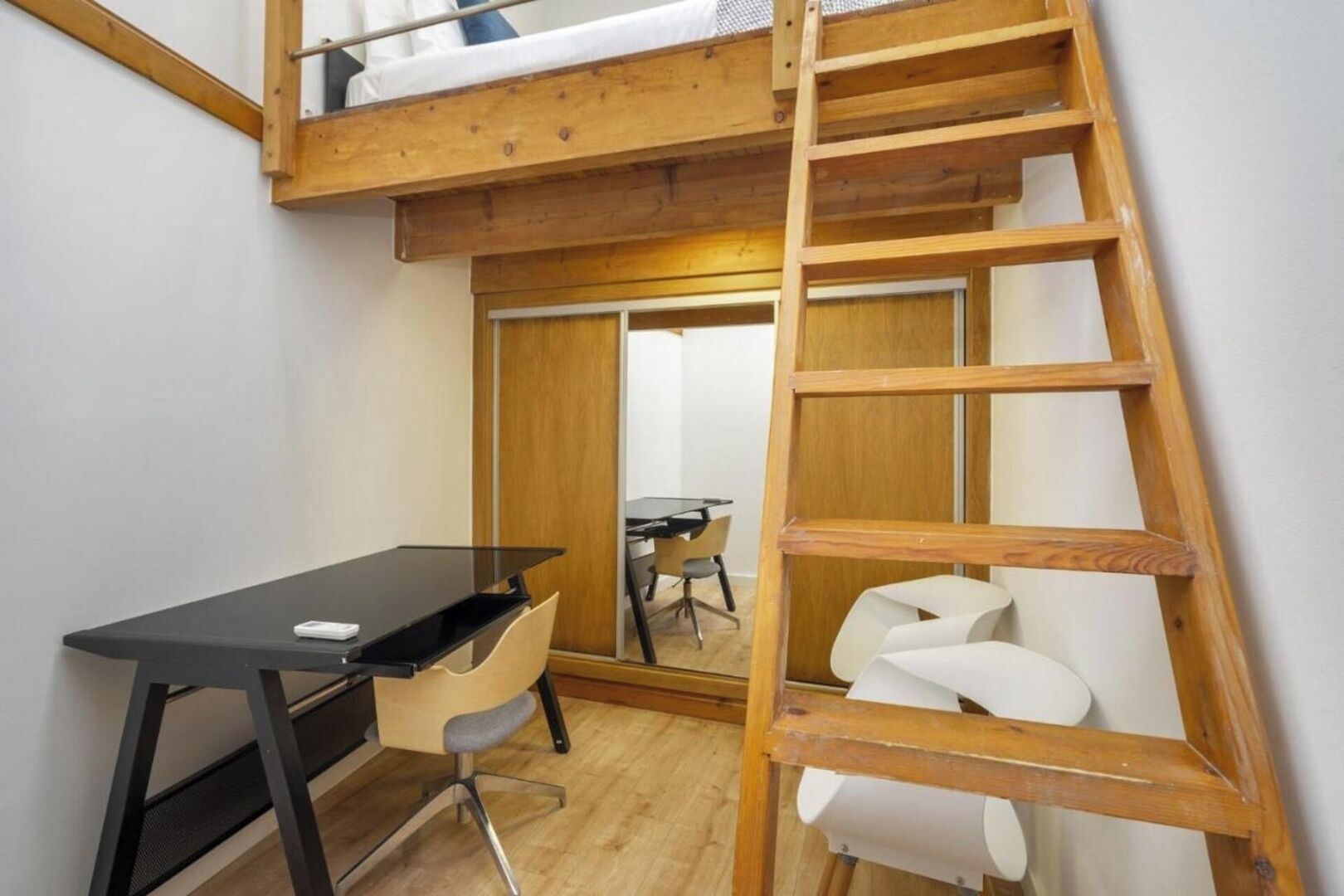 Habitación compacta con cama tipo litera, un escritorio y una silla. Una escalera de madera da acceso a la cama superior.