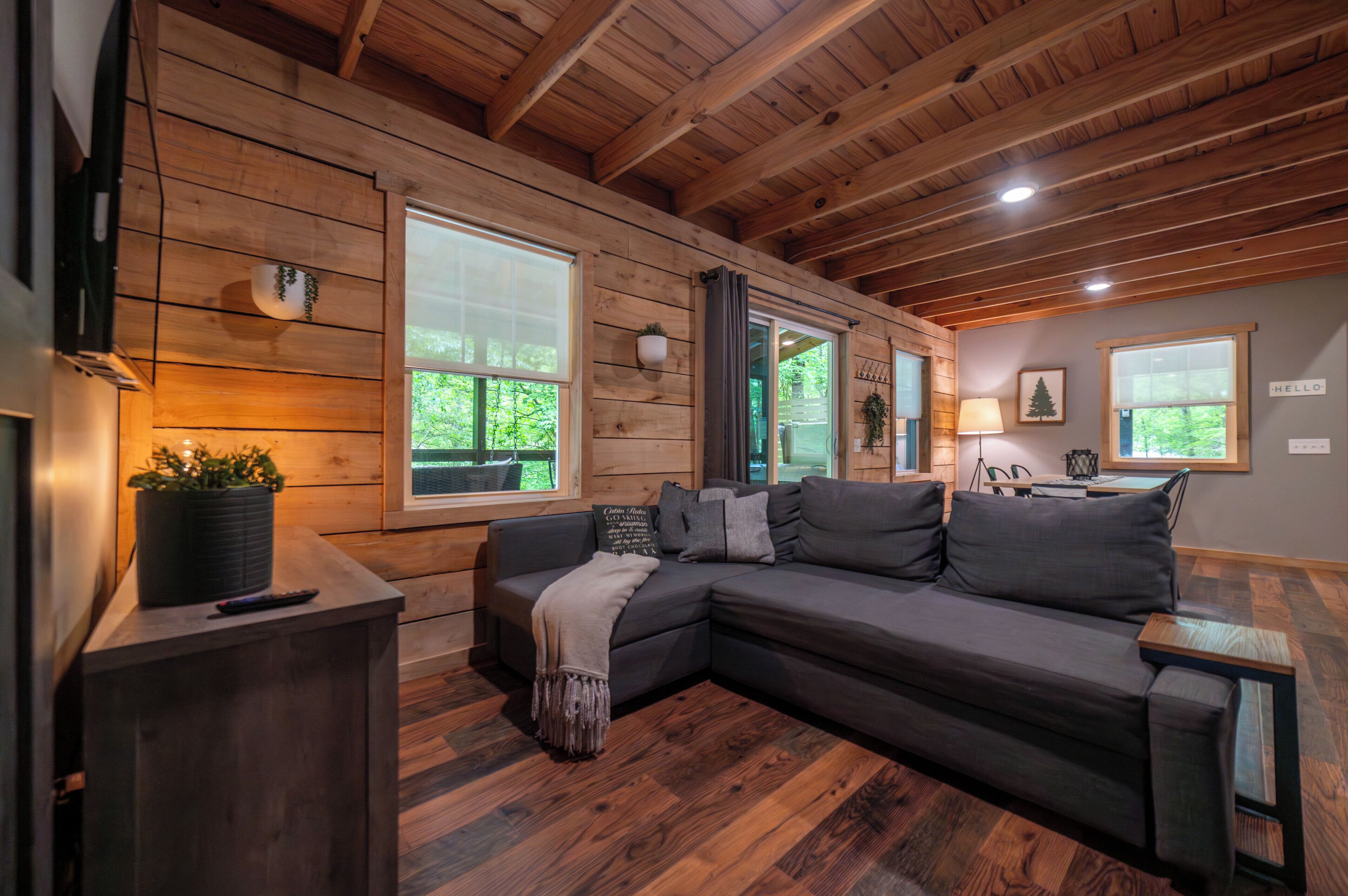 L’intérieur d’un chalet accueillant, avec un plafond en bois, un canapé d’angle, une petite table et une fenêtre donnant sur un paysage verdoyant.