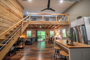 A spacious loft-style room with a wooden floor, a mezzanine with a balcony, a kitchen area, and a dining space.