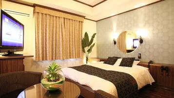 A hotel room with a bed, a television, a round table with a plant, and a mirror on the wall.