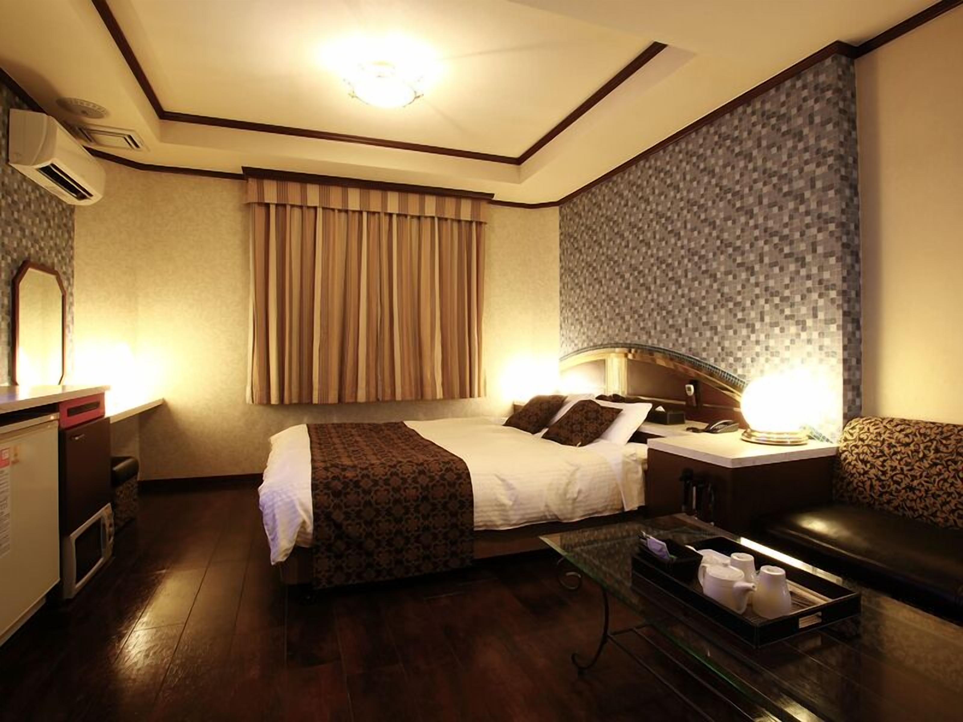 A hotel room with a bed, bedside table, lamp, and a small seating area.