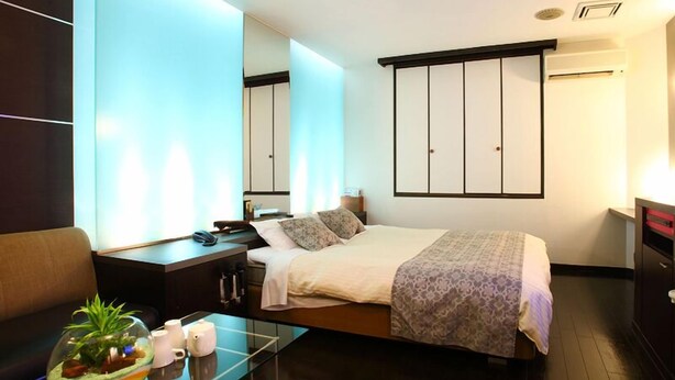 Une chambre d’hôtel moderne, équipée d’un lit, d’une table de chevet et d’une table basse en verre agrémentée d’une plante.