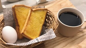 Un panier contenant deux tranches de pain grillé, un œuf dur et une tasse de café noir, le tout posé sur un plateau en bois.
