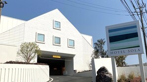 Un bâtiment moderne à la façade blanche et au toit triangulaire, portant l’inscription « HÔTEL SOLA ».